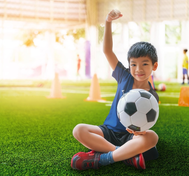 Little soccer boy showing confidence triumph hand on football training ground