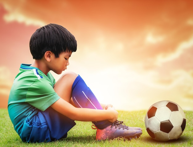 Little soccer football playing is sitting sadly with football on his side after losing a sport game