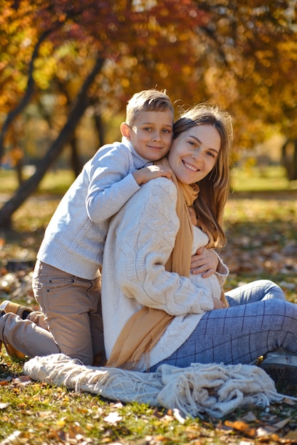 Little son hugs his pregnant mom on the nature. boy and smiling pregnant woman sitting in Autumn park. young happy family waiting baby. pregnant woman enjoying time with her child