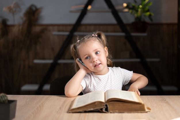 Little student preschool elementary school schooled at home and talking on the phone while sitting at a desk Pupil learning at home school doing homework Technology and education for children