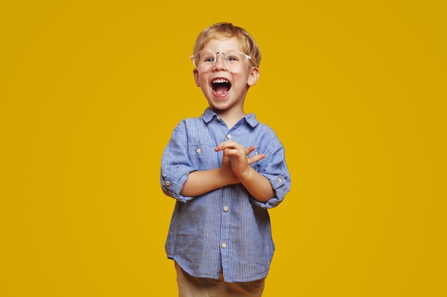 Photo little surprised child wearing striped blue shirt and stylish glasses clapping hands and yelling in