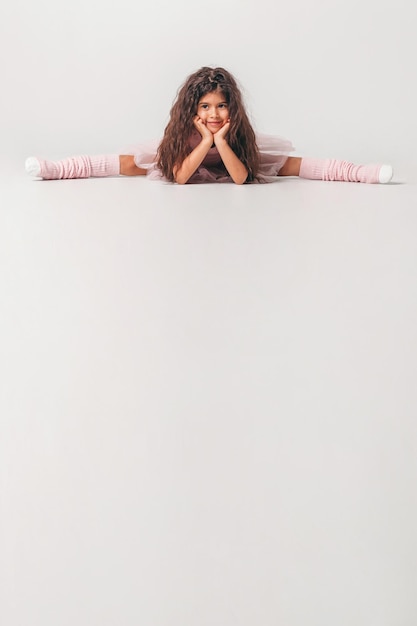 Little swarthy ballerina dancer in a pink tutu academy student posing on white background