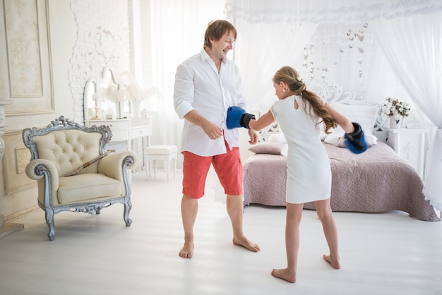 Little teenage girl fights with her dad using boxing gloves while standing in a chic living room with beautiful decor