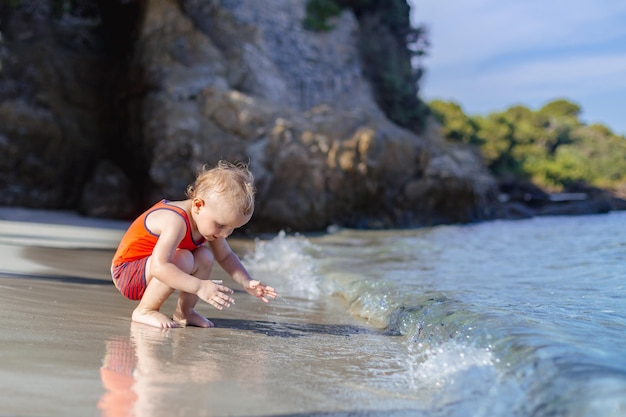 Little toddler boy playing with water on a beach. Child wearing sun protection clothes. Summer vacation in France. Holidays with children concept, copy space.