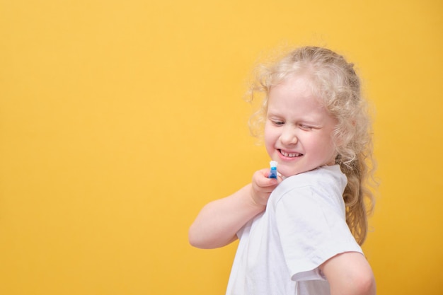 Little toddler girl 6 years old holding toothbrush in hand brushing tooth yellow background