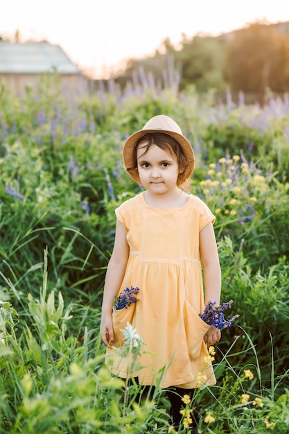 Little toddler girl in a yellow dress walking and picking flowers on a meadow field