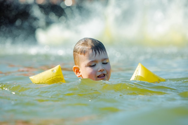 Little toddler kid swimming in lake with inflatable arms aids support summer lake