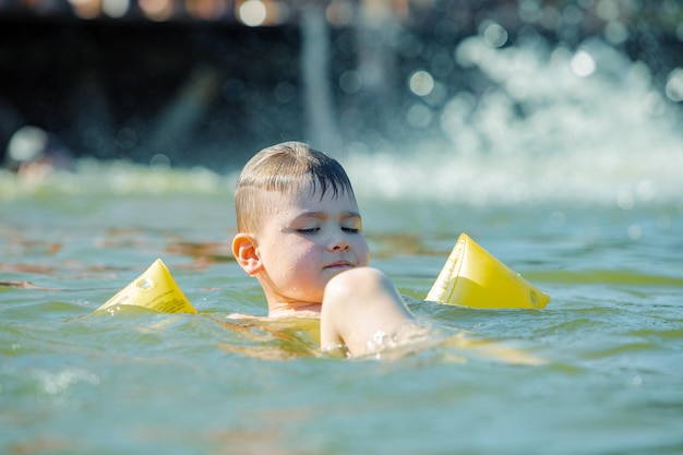 Little toddler kid swimming in lake with inflatable arms aids support