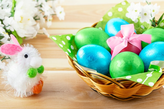 Little Toy Bunny On Wooden table and  Basket With Decorated Eggs