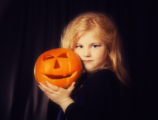 Little witch with pumpkin on dark background