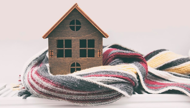 The little wooden house wrapped in the scarf lying on the radiator in the house