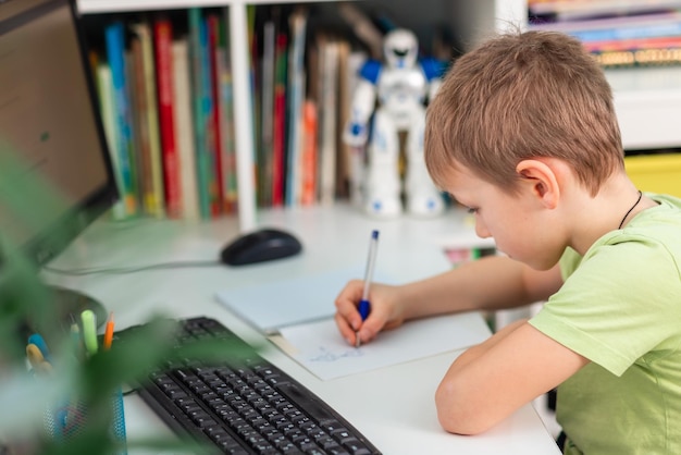 Little young school boy working at home with a laptop and class notes studying in a virtual class Distance education and learning elearning online learning concept during quarantine