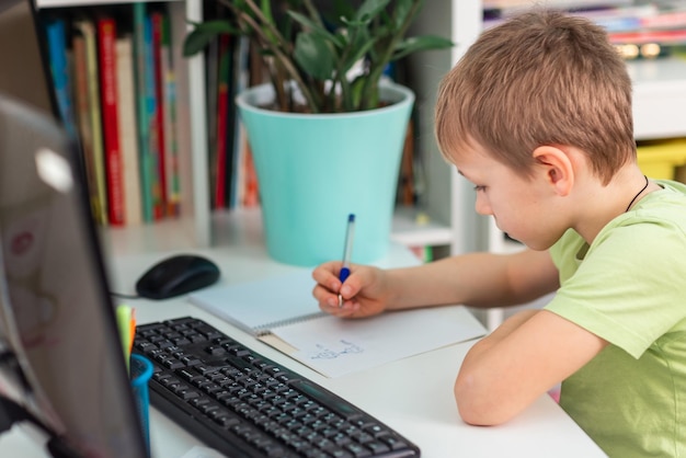 Little young school boy working at home with a laptop and class notes studying in a virtual class Distance education and learning elearning online learning concept