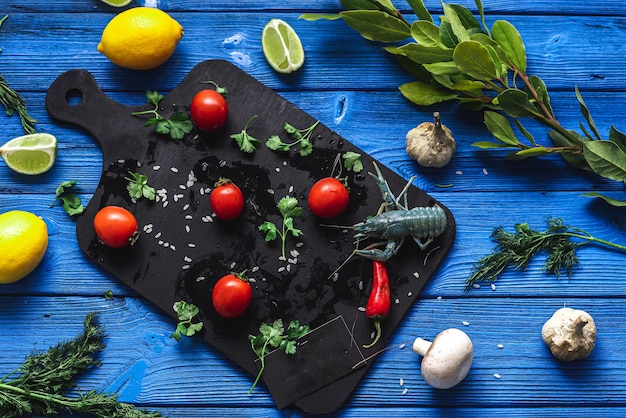 Live crayfish on a black cutting board, on a blue background of different colors next to vegetables and greens