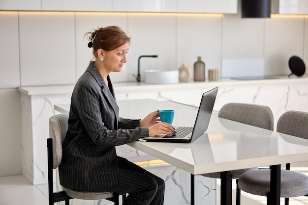 Live streaming virtual classes by businesswoman in suit with laptop in kitchen.