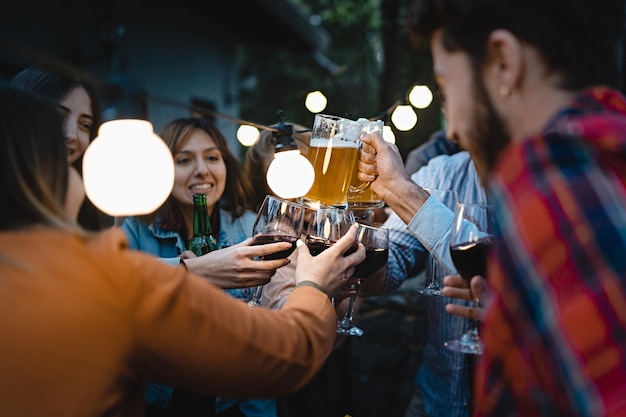 A lively group of friends toasting in the terrace of the restaurant pub in the countryside under the lights outdoors concept of people having fun drinking and eating together on summer weekends