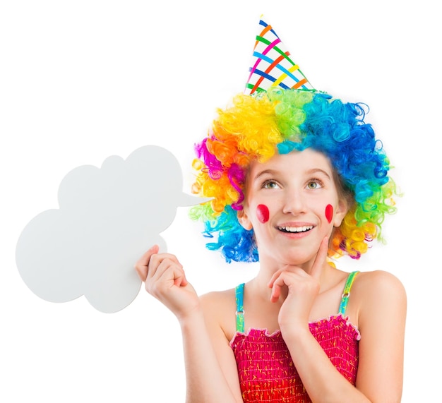 Lively little girl in bright colouful clown wig holding white speech bubble isolated on white backgr