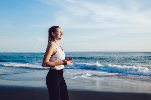 Lively woman listening music on smartphone at seaside