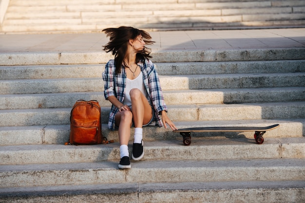 Lively woman sitting on the stairs next to her skateboard shaking head