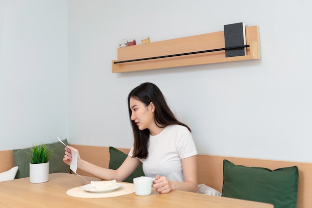 Living room concept a pretty lady holding a paper to read while another hand holding a cup of caffeine beverage in the living room.