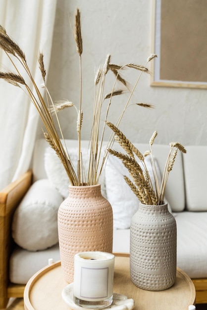 Living room decor Dry wheat stands in ceramic vases on a wooden table next to a cozy light sofa