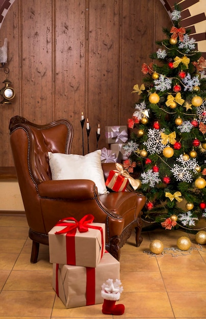 The living room in the house is decorated for Christmas Christmas tree decorated for the holiday and a lot of gifts next to it Retro armchair in the house