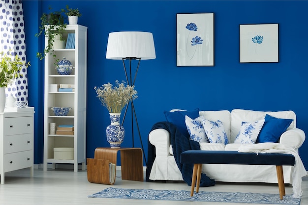 A living room with a blue and white couch and a white shelf with a vase of flowers on it.