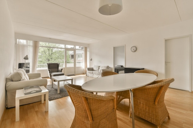 a living room with white walls and wood flooring including a round dining table surrounded by wickers