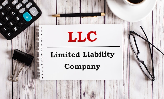 Photo llc limited liability company is written in a white notepad near a calculator, coffee, glasses and a pen