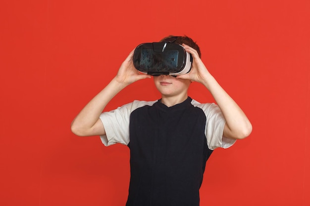 Llittle boy in virtual reality glasses playing the game on a red background 3D gadget technology Cardboard VR headset glasses