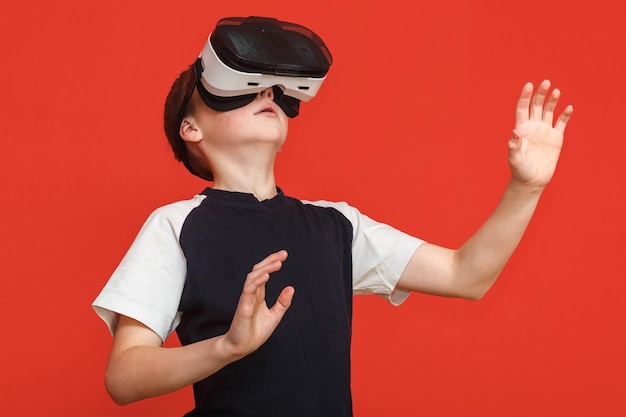 Llittle boy in virtual reality glasses playing the game on a red background 3D gadget technology Cardboard VR headset glasses