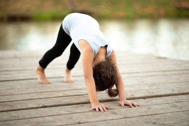 Llittle girl sitting in nature near by river or lake and practicing yoga Healthy lifestyle