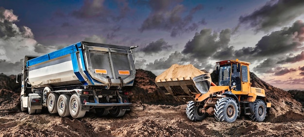 A loader or bedozer loads a dump truck car with sand at a construction site Loading a vehicle for transporting soil A loader or bulldozer moves the soil equipment for earthworks