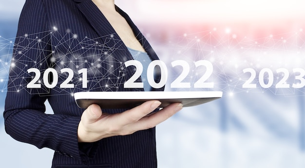 Loading year 2021 to 2022. Start concept. Hand hold white tablet with digital hologram 2022 sign on light blurred background. Concept Start New Year 2022.