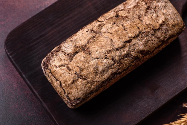 A loaf of brown bread with grains of cereals on a wooden cutting board