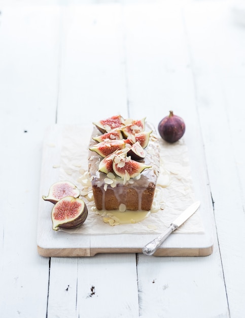 Loaf cake with figs, almond and white chocolate on wooden serving board over grunge surface, selective focus.