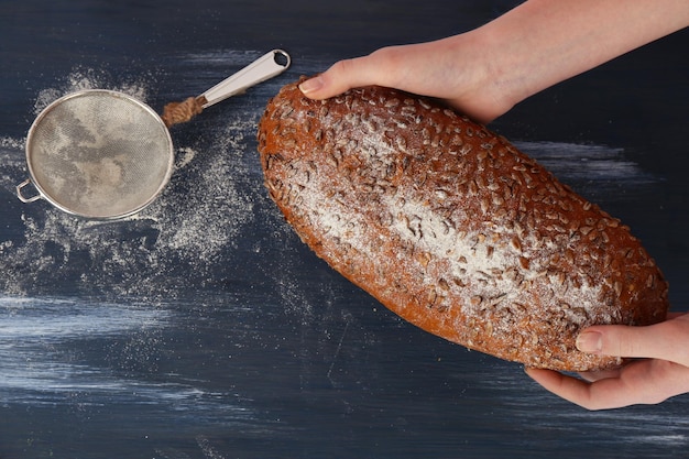 Loaf of freshly bread in female hands on color wooden table background