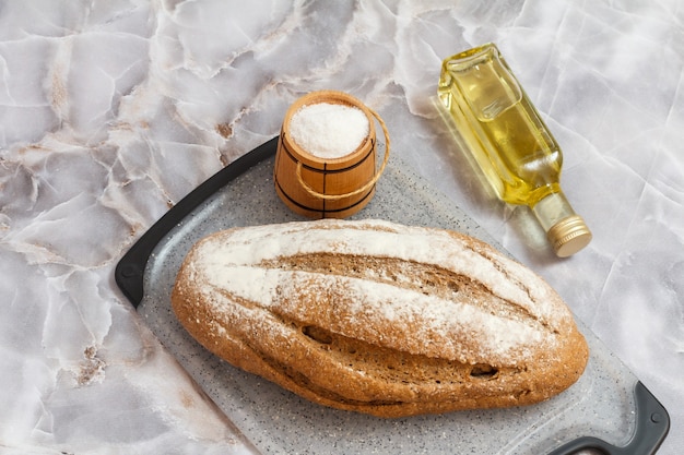 loaf of rye bread on a cutting board, a bottle of sunflower oil and a wooden salt cellar