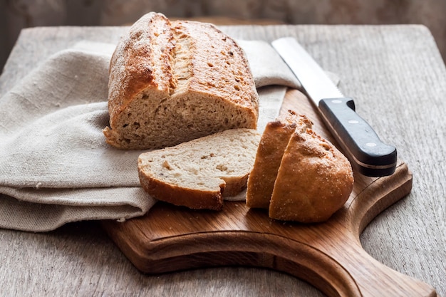 Loaf of whole wheat bread with slices on wooden board on kitchen table