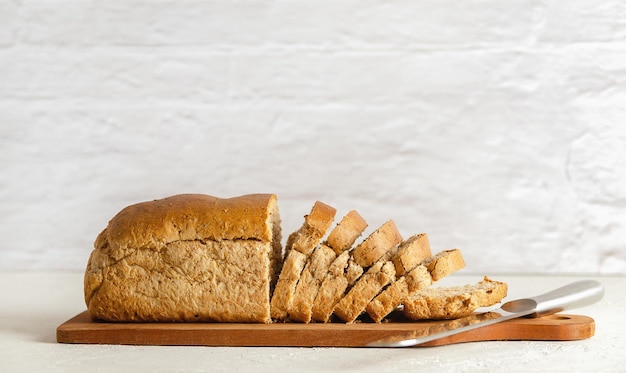 A loaf of wholemeal bread on a wooden cutting board with a knife on white background