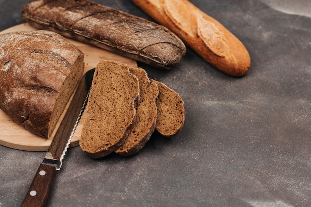 Loafs of rye and wheat bread on a wooden board. Bread slices and knife.