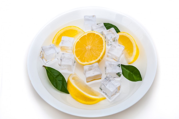 Lobes of fresh, juicy, bright, yellow lemon, cubes of refreshing ice and green leaves 