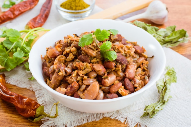 Lobio - the national Georgian dish of beans in a white plate and the ingredients for its preparation on a wooden table