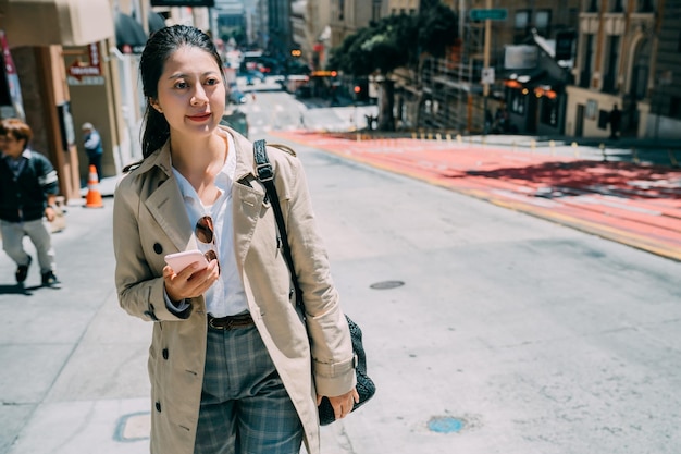 local lifestyle concept. Portrait of beautiful young asian japanese woman using her mobile phone walking in city street in california usa. girl on sunshine spring day relaxing shopping in urban