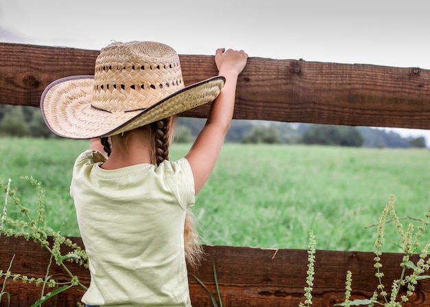 Photo local vacation, stay safe, stay home. little girl in cowboy hat playing in western in the farm among mountains, happy summertime in the countryside, childhood and dreams