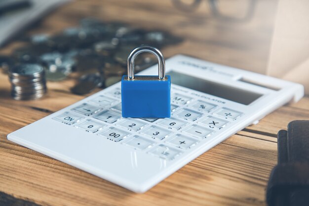 Lock on calculator next to coins arrangement on wooden table