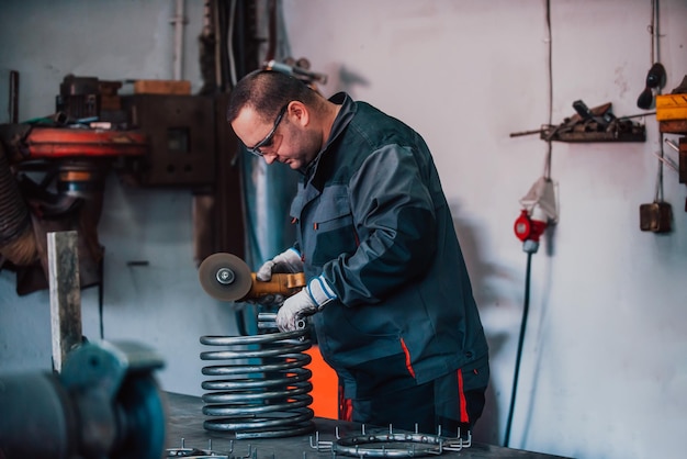 Locksmith in special clothes and goggles works in production metal processing with angle grinder spa