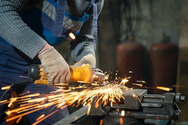 Locksmith in special clothes and goggles works in production. Metal processing with angle grinder