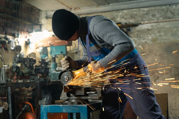 Locksmith in special clothes and goggles works in production metal processing with angle grinder