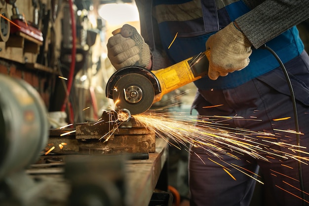 Locksmith in special clothes and goggles works in production metal processing with angle grinder